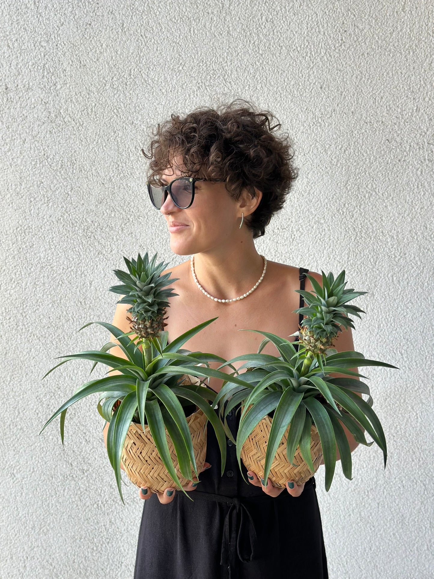 An elegant woman holding two pineapple plants in woven baskets, showcasing luxury indoor greenery | Элегантная женщина держит два ананасовых растения в плетёных корзинах, демонстрируя роскошное домашнее озеленение | An elegant woman holding two pineapple plants in woven baskets, showcasing luxury indoor greenery
