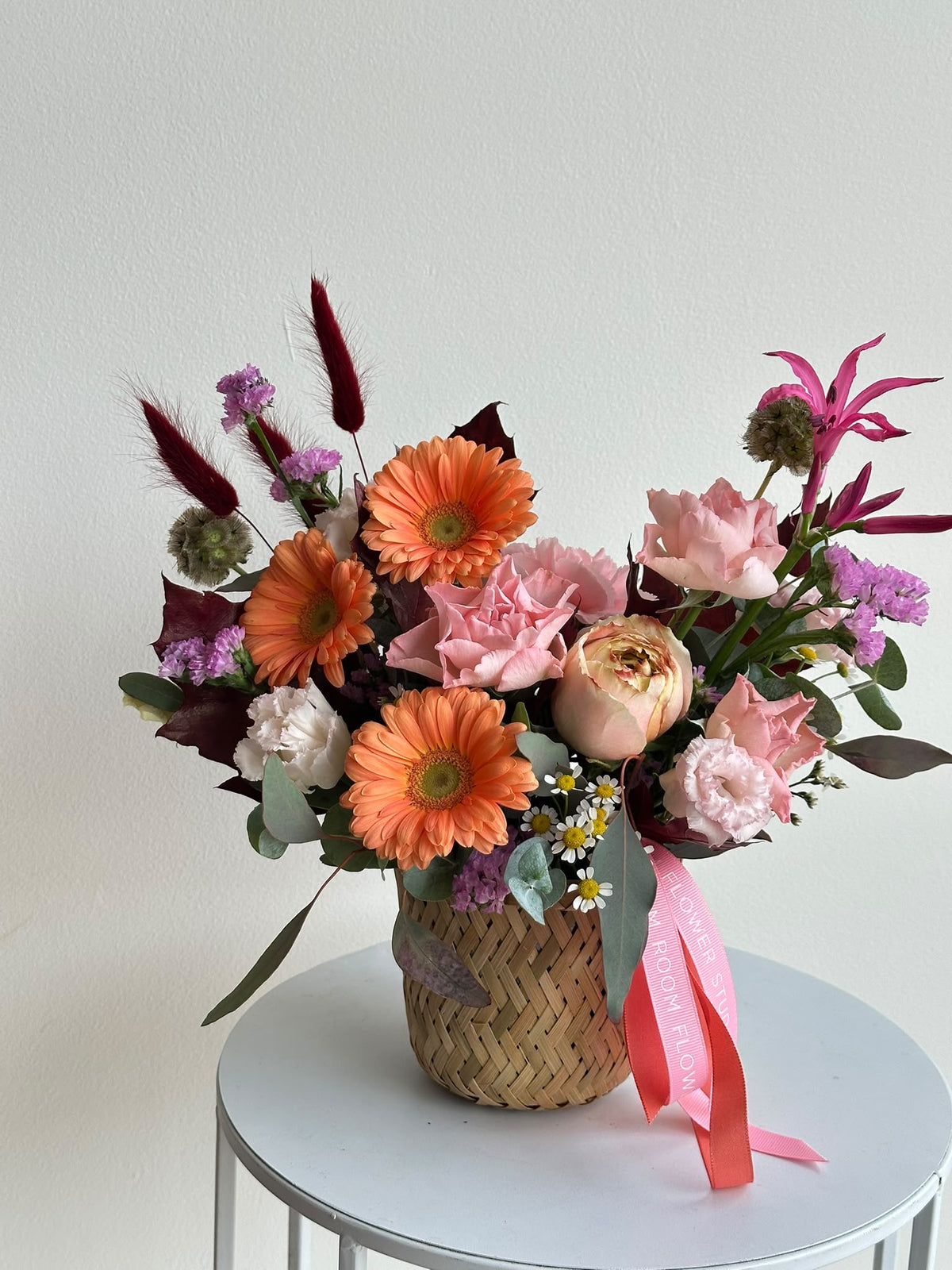 “Autumn Embrace” flower basket with orange gerberas, pink carnations, eustoma, limonium and autumn leaves in a woven basket