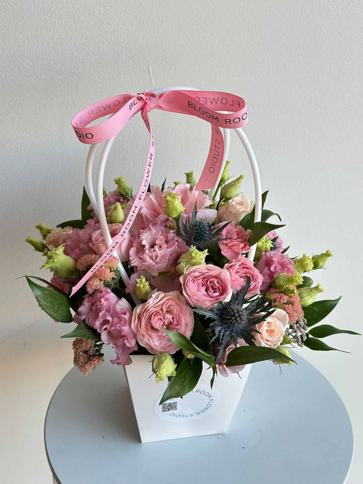 “Petite Romance” mini flower bag with pink spray roses, carnations, eustoma and eryngium in a white Bloom Room bag