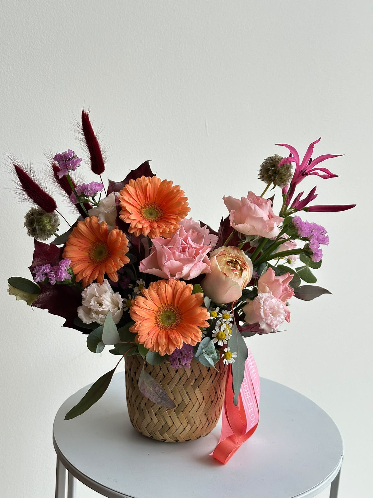 “Autumn Embrace” flower basket with orange gerberas, pink carnations, eustoma, limonium and autumn leaves in a woven basket
