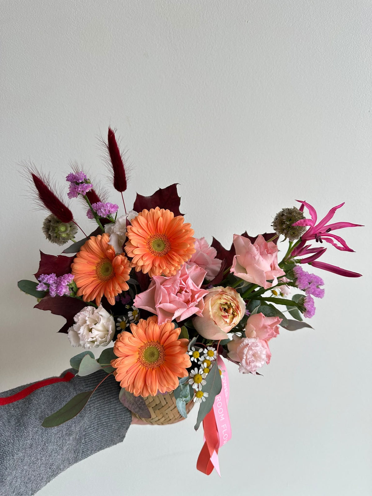 “Autumn Embrace” flower basket with orange gerberas, pink carnations, eustoma, limonium and autumn leaves in a woven basket