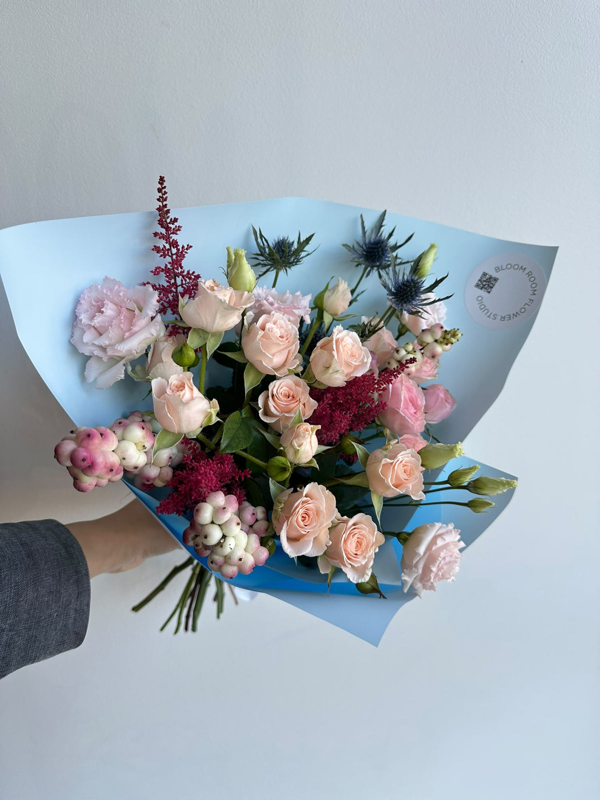 „Blue Serenade“ floristi kimp virsikukarva ja roosade kobarrooside, preeriakella, astilbe, ogaputke ja lumimarjadega taevasinises pakendis