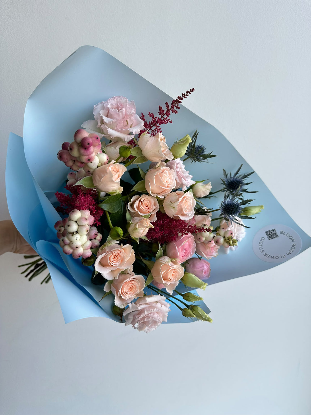 „Blue Serenade“ floristi kimp virsikukarva ja roosade kobarrooside, preeriakella, astilbe, ogaputke ja lumimarjadega taevasinises pakendis