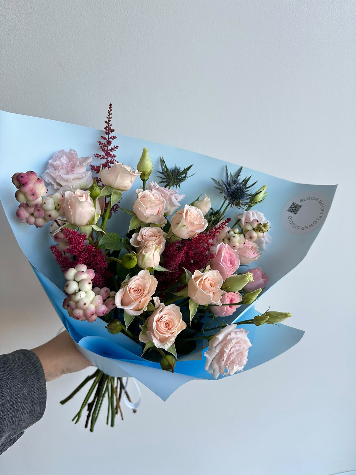 „Blue Serenade“ floristi kimp virsikukarva ja roosade kobarrooside, preeriakella, astilbe, ogaputke ja lumimarjadega taevasinises pakendis