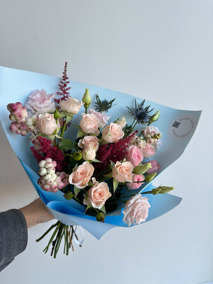 „Blue Serenade“ floristi kimp virsikukarva ja roosade kobarrooside, preeriakella, astilbe, ogaputke ja lumimarjadega taevasinises pakendis