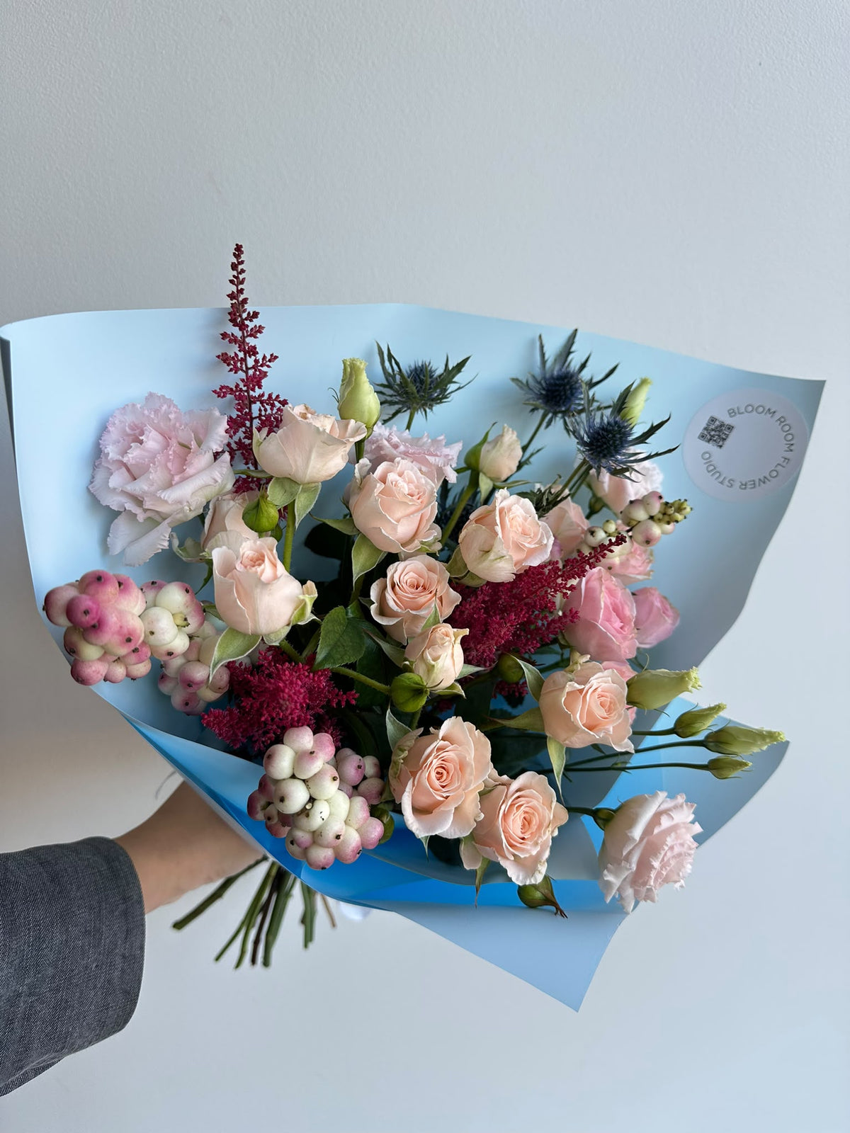 „Blue Serenade“ floristi kimp virsikukarva ja roosade kobarrooside, preeriakella, astilbe, ogaputke ja lumimarjadega taevasinises pakendis