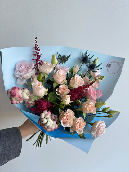 „Blue Serenade“ floristi kimp virsikukarva ja roosade kobarrooside, preeriakella, astilbe, ogaputke ja lumimarjadega taevasinises pakendis