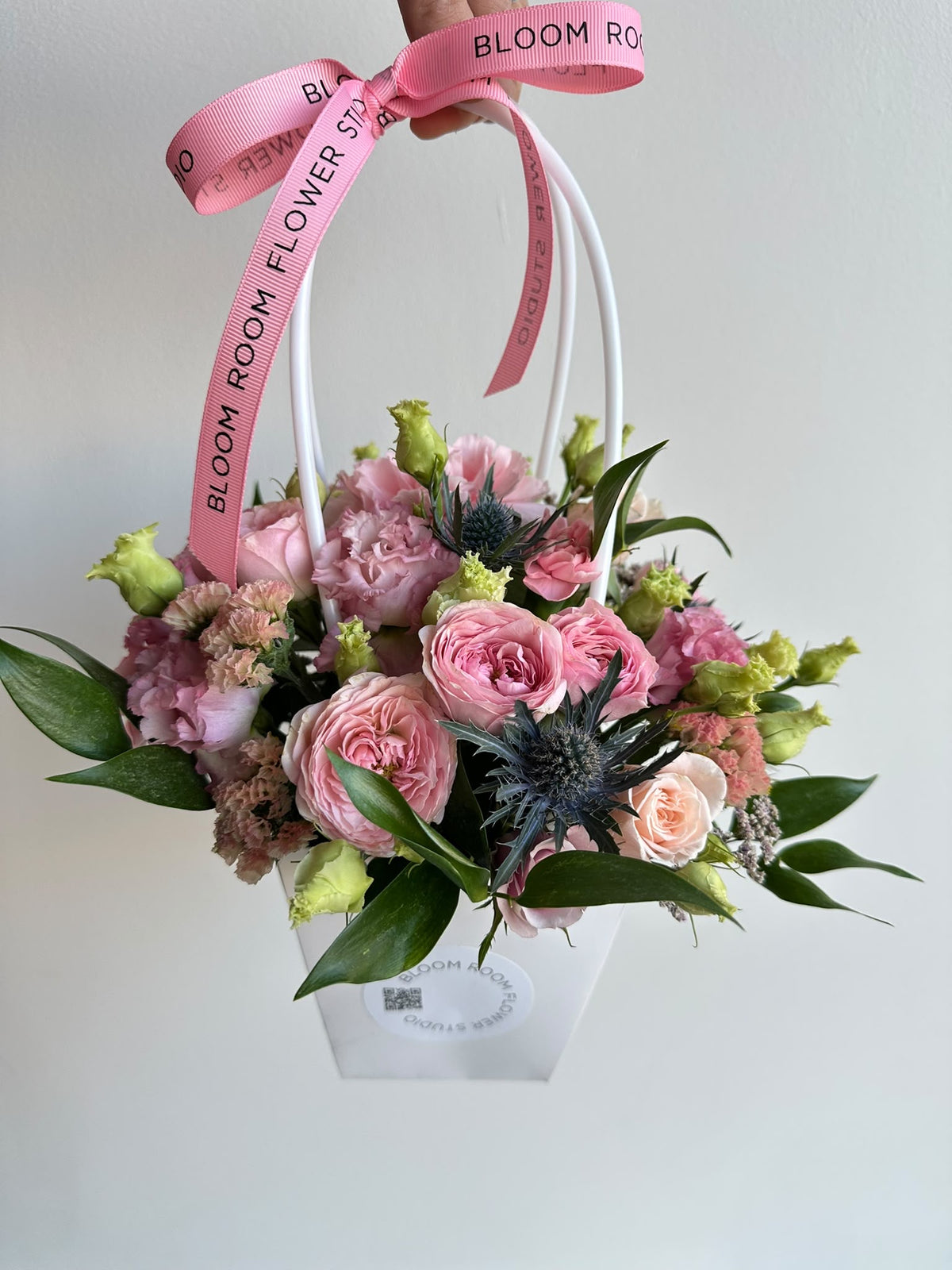 “Petite Romance” mini flower bag with pink spray roses, carnations, eustoma and eryngium in a white Bloom Room bag
