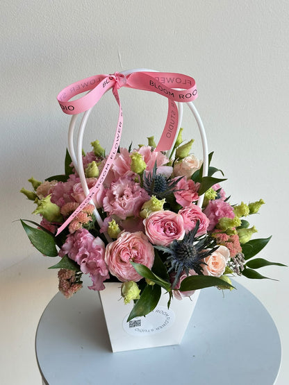“Petite Romance” mini flower bag with pink spray roses, carnations, eustoma and eryngium in a white Bloom Room bag