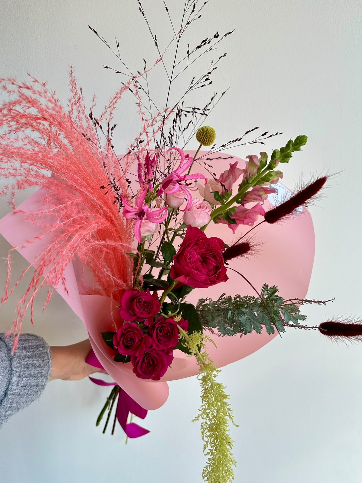 “Pink Rhapsody” art bouquet with garden rose, cerise spray roses, nerine, snapdragons and coral pampas grass in pink wrapping