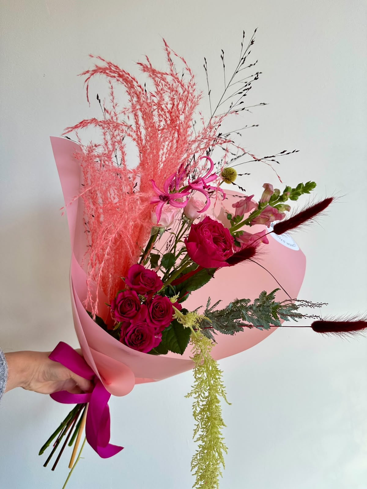 “Pink Rhapsody” art bouquet with garden rose, cerise spray roses, nerine, snapdragons and coral pampas grass in pink wrapping