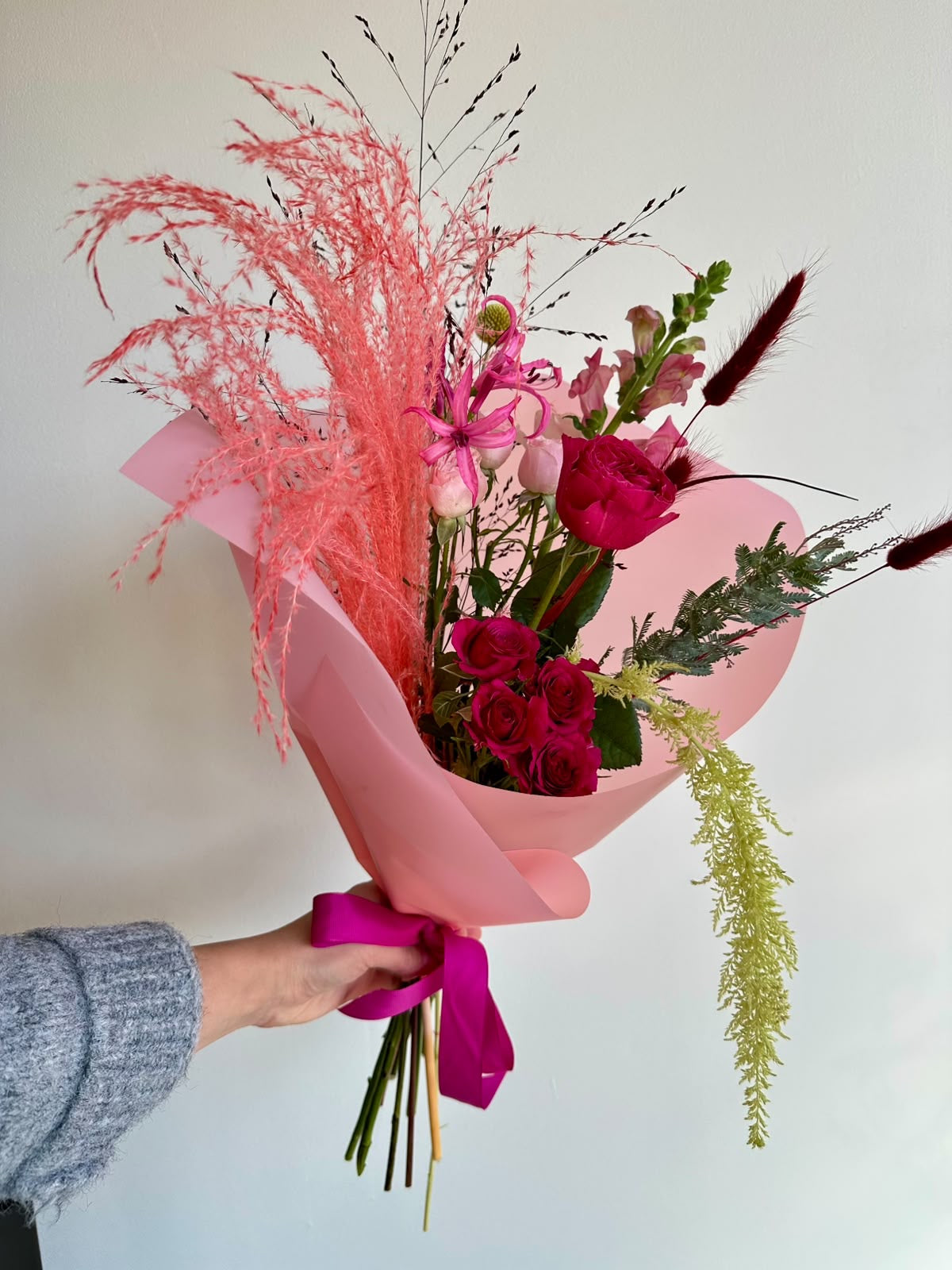 “Pink Rhapsody” art bouquet with garden rose, cerise spray roses, nerine, snapdragons and coral pampas grass in pink wrapping