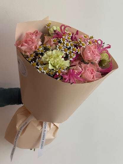 „Sweet Serenade“ floristi kimp roosade kobarrooside, roheliste nelkide, roosa nerine ja kummeliga kreemikas pakendis